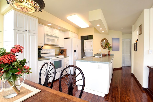 kitchen with white cabinets, dark hardwood / wood-style flooring, white appliances, and stacked washer / dryer