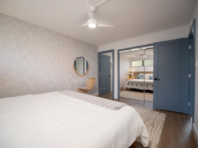 bedroom featuring ceiling fan, a textured ceiling, a closet, dark wood-style floors, and wallpapered walls