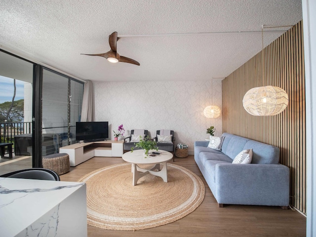 living room featuring wallpapered walls, ceiling fan, a textured ceiling, and wood finished floors