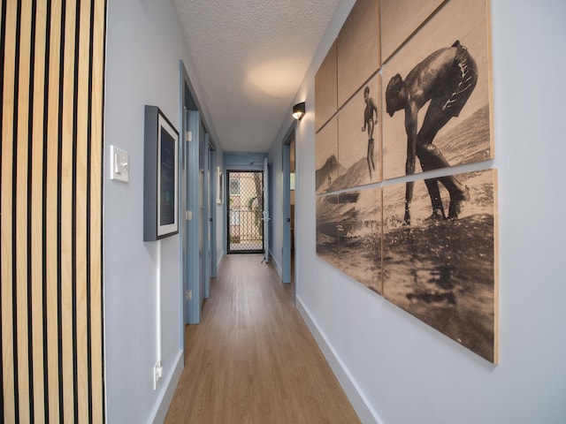 corridor with light wood-style flooring, a textured ceiling, and baseboards