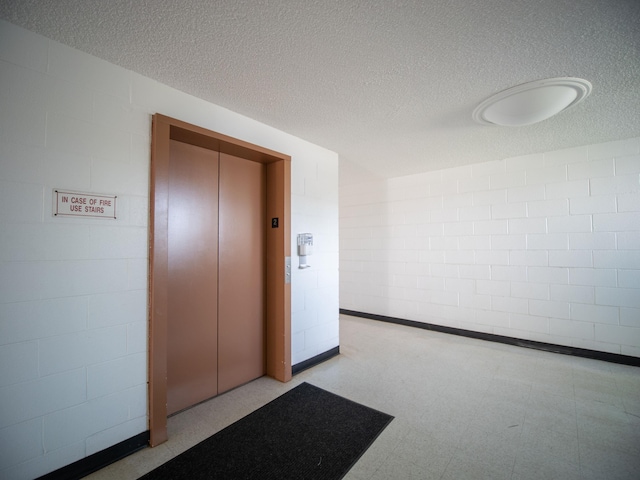 hall featuring a textured ceiling, tile patterned floors, concrete block wall, and elevator