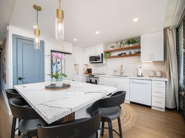 kitchen with light wood-style flooring, white appliances, a breakfast bar, a kitchen island, and a sink