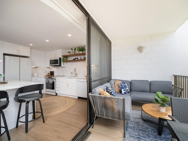 interior space with white appliances, white cabinets, light wood-style flooring, light countertops, and a sink