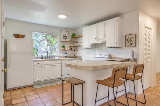 kitchen with tile countertops, white appliances, a breakfast bar area, and white cabinetry