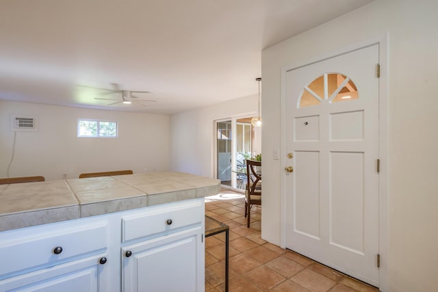 kitchen with tile countertops, ceiling fan, a breakfast bar, hanging light fixtures, and white cabinetry