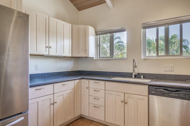 kitchen with light tile patterned floors, a sink, vaulted ceiling, appliances with stainless steel finishes, and dark countertops