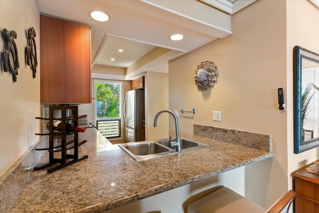 kitchen with kitchen peninsula, stainless steel fridge, sink, and light stone counters