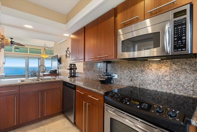 kitchen with tasteful backsplash, dark stone countertops, stainless steel appliances, ceiling fan, and sink