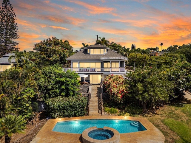 back house at dusk with a swimming pool with hot tub