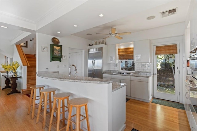 kitchen with stainless steel appliances, kitchen peninsula, backsplash, white cabinetry, and light wood-type flooring