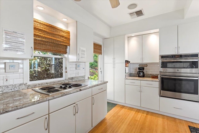 kitchen with light hardwood / wood-style floors, tasteful backsplash, double oven, white stovetop, and white cabinets