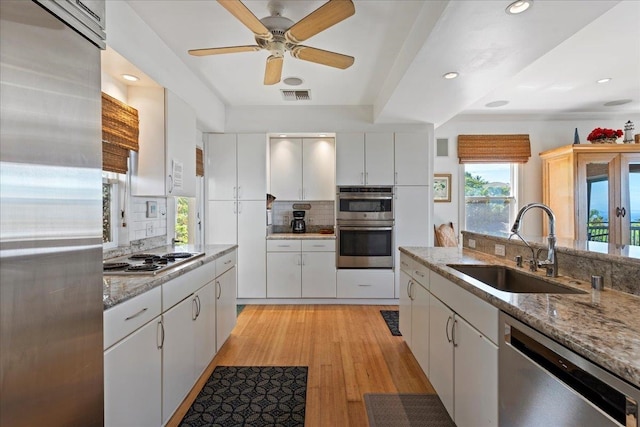 kitchen featuring tasteful backsplash, stainless steel appliances, white cabinetry, sink, and light hardwood / wood-style flooring