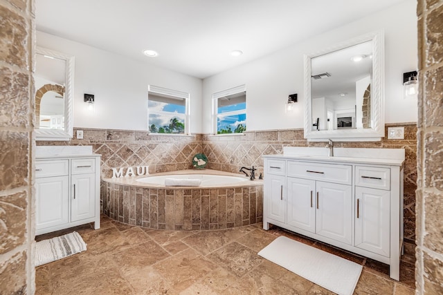 bathroom featuring two vanities, tile walls, a garden tub, and visible vents