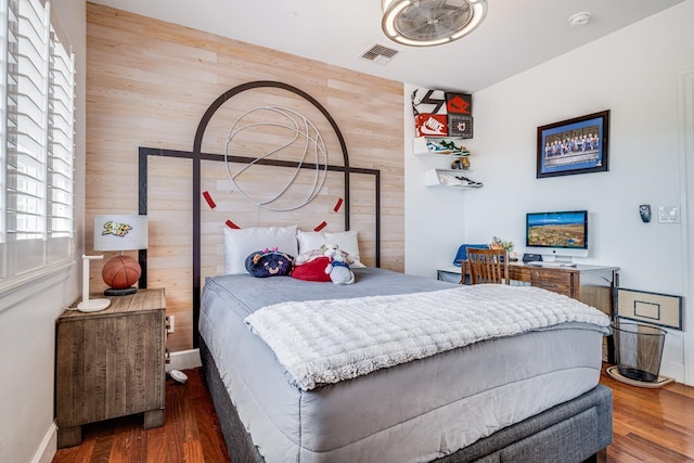 bedroom with visible vents, wood finished floors, baseboards, and wood walls