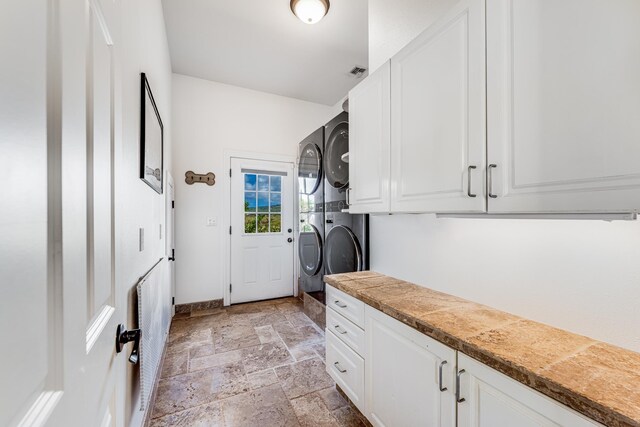 laundry room with baseboards, visible vents, cabinet space, stone tile flooring, and stacked washer and dryer