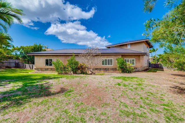 rear view of property featuring stucco siding, a lawn, and fence