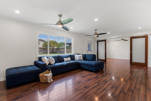 living room featuring dark hardwood / wood-style floors, ceiling fan, ornamental molding, and a barn door