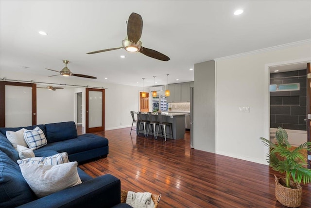 living room featuring crown molding, a barn door, dark wood-type flooring, and ceiling fan