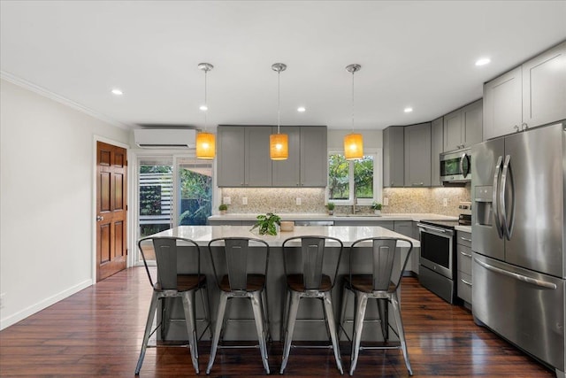 kitchen with gray cabinets, appliances with stainless steel finishes, an AC wall unit, backsplash, and a center island