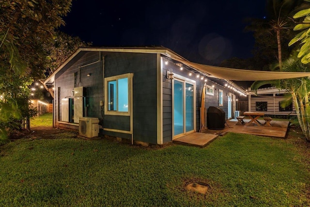 back house at night featuring a yard and ac unit