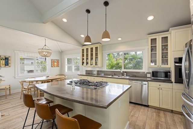 kitchen with a sink, light wood-style floors, appliances with stainless steel finishes, and vaulted ceiling with beams