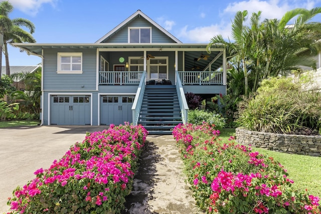 raised beach house with stairway, a porch, concrete driveway, an attached garage, and a ceiling fan