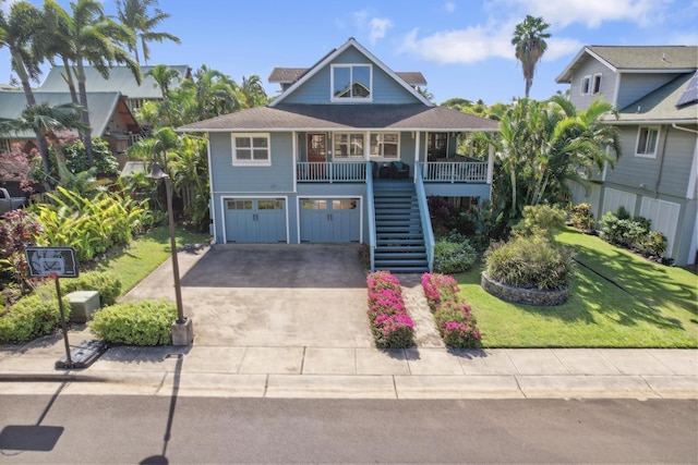 raised beach house with a front yard, stairway, a porch, concrete driveway, and a garage