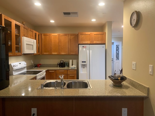 kitchen with white appliances, kitchen peninsula, light stone countertops, and sink