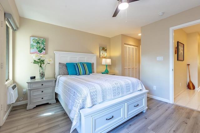 bedroom with ceiling fan, light wood-type flooring, a wall mounted AC, and a closet