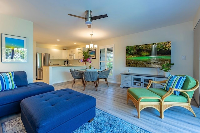 living room featuring ceiling fan with notable chandelier and light hardwood / wood-style floors