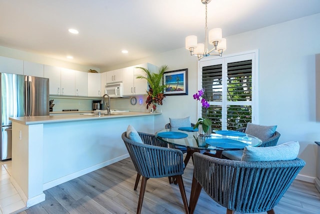 kitchen featuring sink, kitchen peninsula, decorative light fixtures, white cabinetry, and stainless steel refrigerator