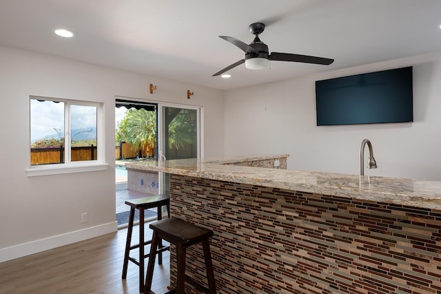 bar with ceiling fan, light stone counters, wood-type flooring, and sink