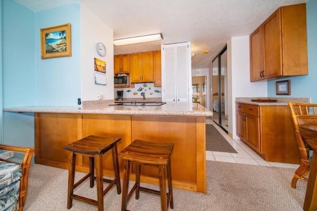 kitchen featuring stainless steel microwave, a breakfast bar area, light carpet, light stone countertops, and kitchen peninsula