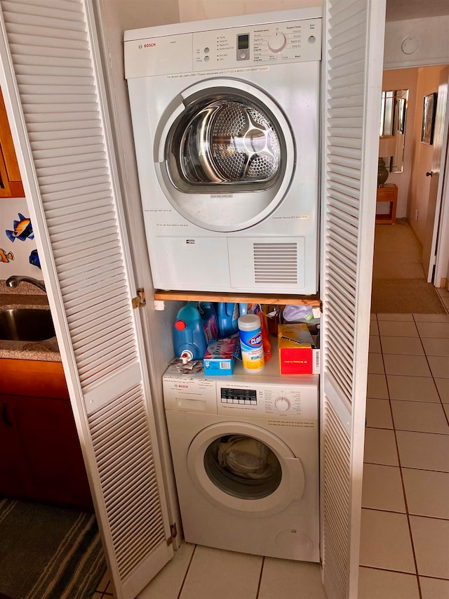 clothes washing area with sink, tile patterned floors, and stacked washer and dryer