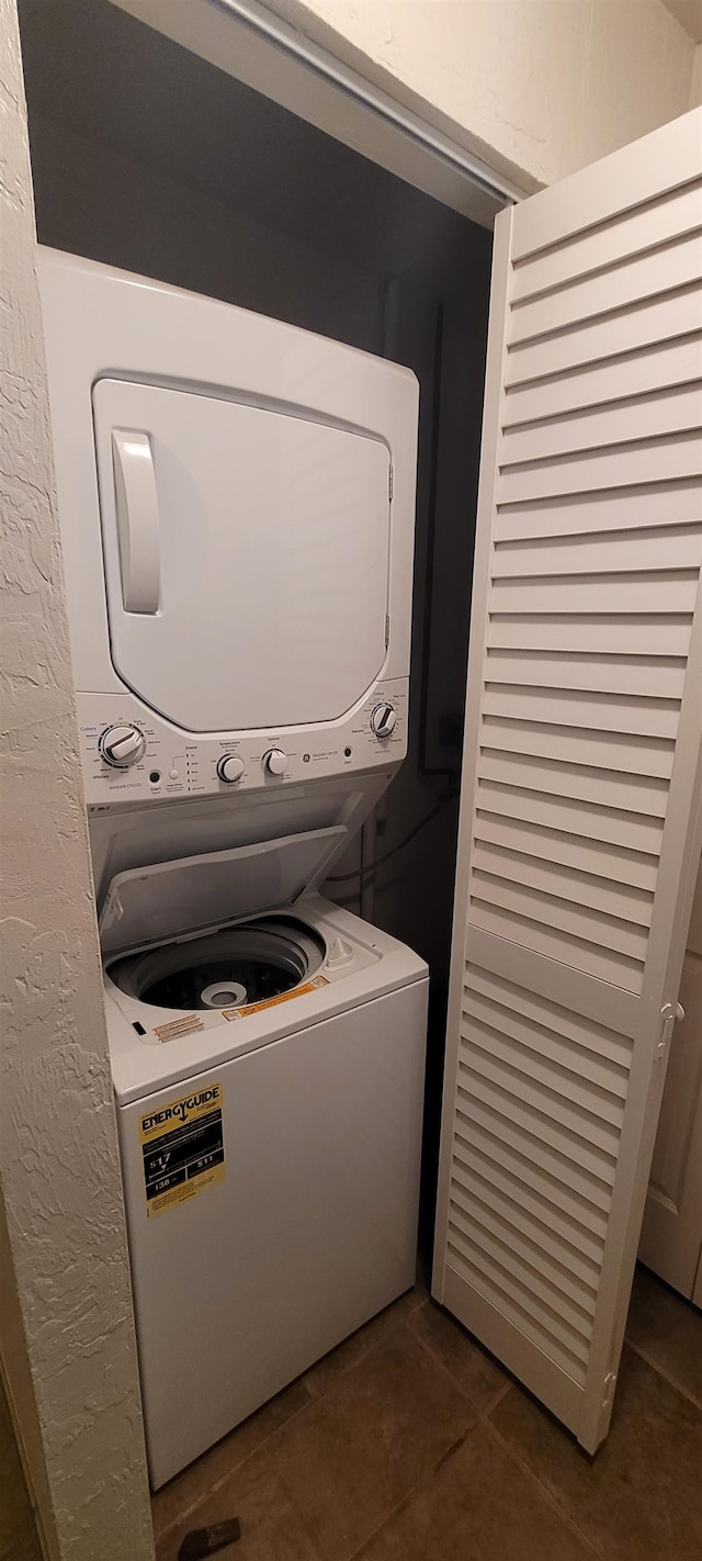 laundry area with dark tile patterned flooring and stacked washer and dryer