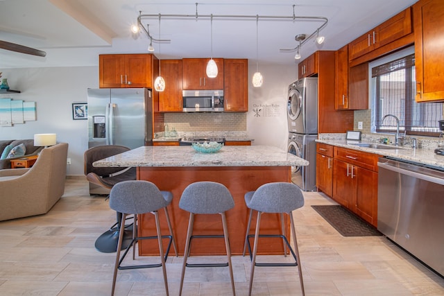 kitchen with sink, a center island, hanging light fixtures, stainless steel appliances, and stacked washer and clothes dryer