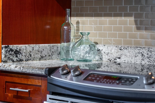 room details with decorative backsplash, light stone countertops, and stainless steel range oven