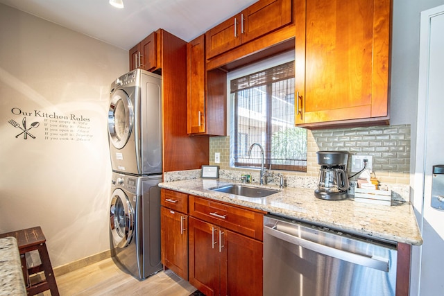 kitchen featuring decorative backsplash, light stone counters, sink, dishwasher, and stacked washer and dryer