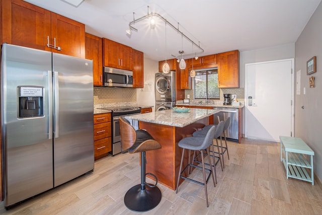 kitchen featuring sink, light stone counters, stacked washer / dryer, a kitchen island, and appliances with stainless steel finishes