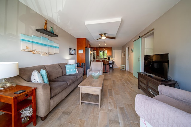 living room with a barn door, ceiling fan, and light wood-type flooring