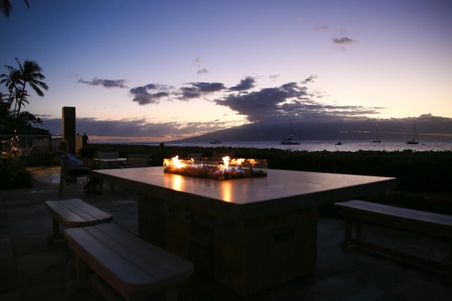 patio terrace at dusk featuring a fire pit and a water view