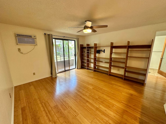 empty room with a wall unit AC, a textured ceiling, light wood-type flooring, and ceiling fan