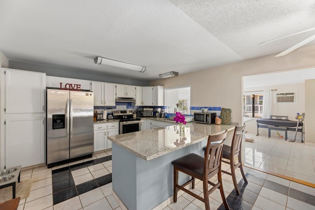 kitchen with a peninsula, light stone countertops, light tile patterned flooring, stainless steel appliances, and a wall mounted AC