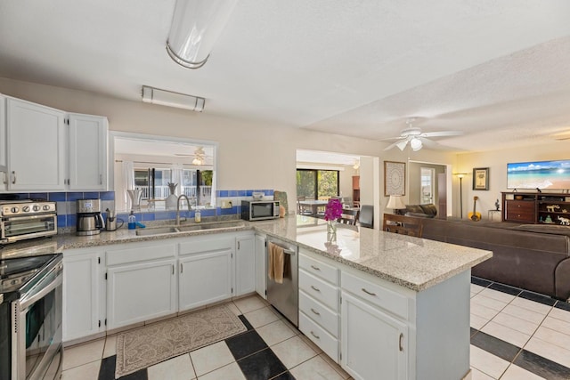 kitchen with appliances with stainless steel finishes, open floor plan, a peninsula, white cabinetry, and a sink