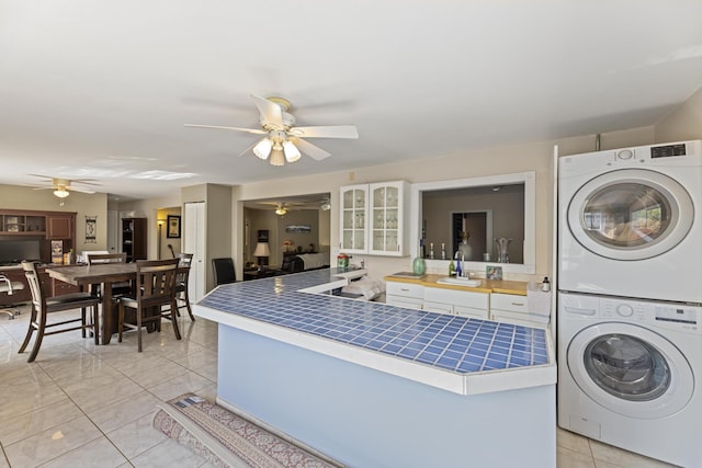 washroom with light tile patterned floors, stacked washer / drying machine, ceiling fan, a sink, and laundry area