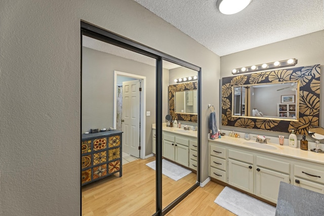 full bath with a textured ceiling, a textured wall, wood finished floors, and vanity