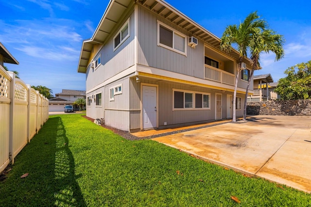 rear view of property with a wall unit AC, a patio area, fence, and a yard