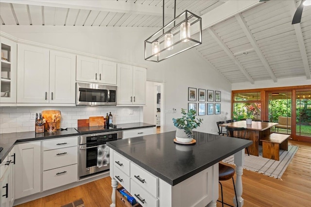 kitchen with appliances with stainless steel finishes, dark countertops, light wood-type flooring, backsplash, and high vaulted ceiling