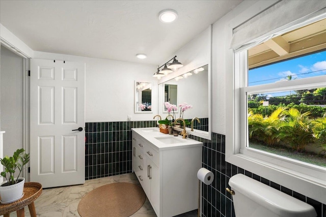 bathroom with tile walls, toilet, marble finish floors, vanity, and a wainscoted wall