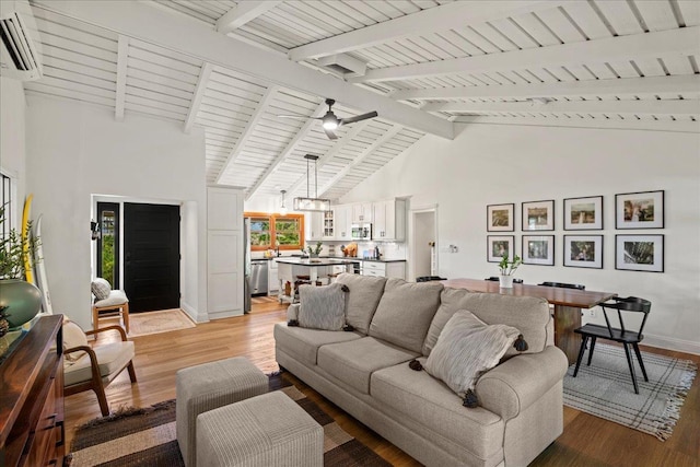 living area with an AC wall unit, beamed ceiling, light wood-type flooring, baseboards, and high vaulted ceiling
